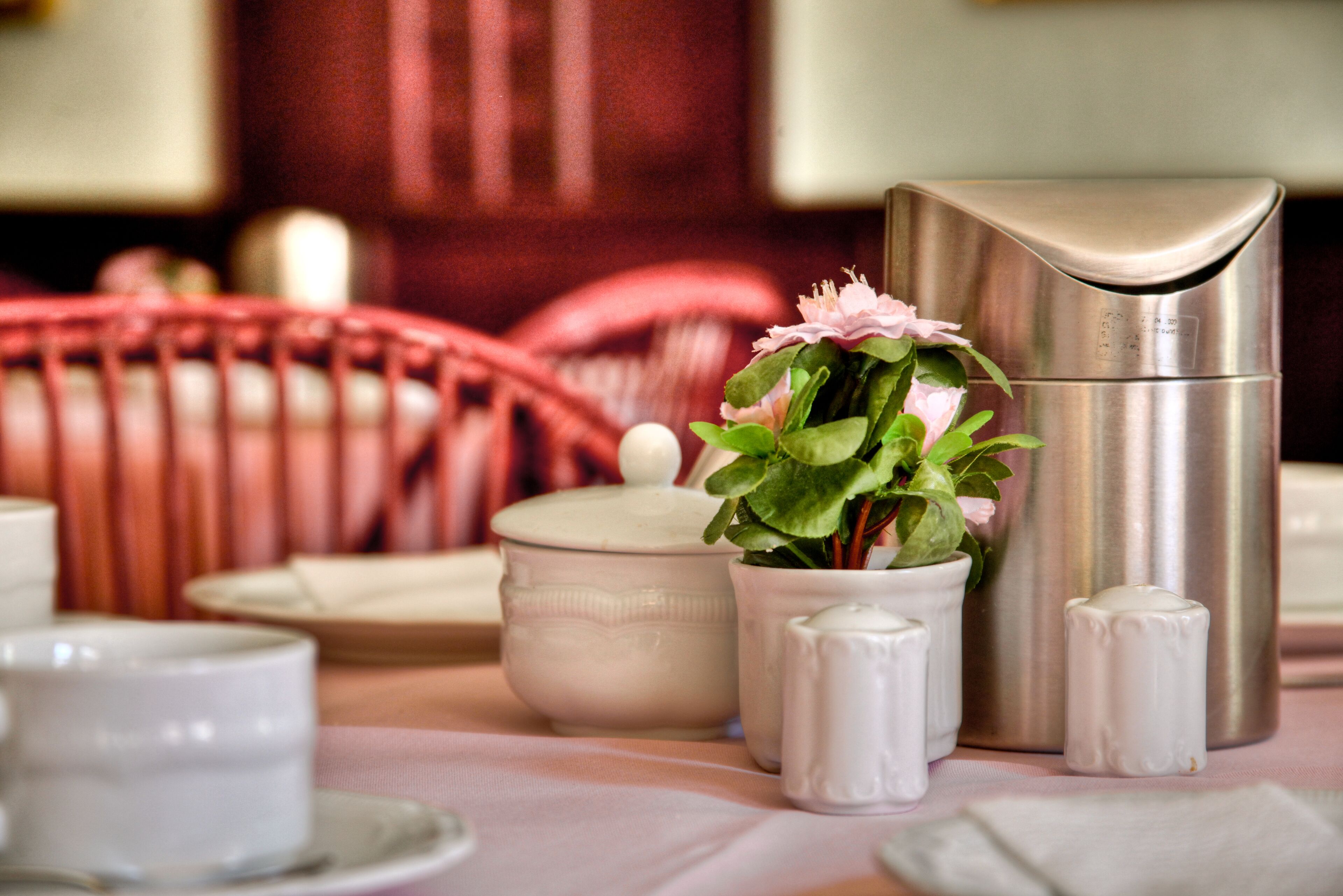Una mesa con un recipiente de acero inoxidable, una maceta de cerámica con flores, saleros y una tetera blanca.
