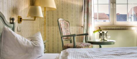 A hotel room with a bed, a chair, a table with a lamp, and a window with curtains.