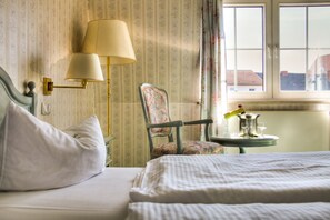 A hotel room with a bed, a chair, a table with a lamp, and a window with curtains.