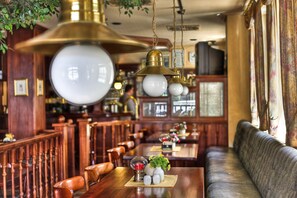 A restaurant with wooden furniture, hanging brass chandeliers, and a long dining table with a floral centerpiece. - Hotel am Markt (Altentreptow)