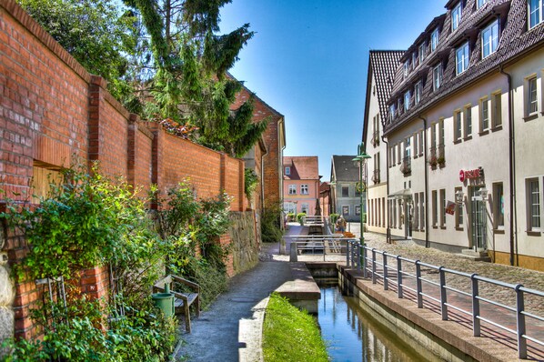 A narrow canal with a brick wall on one side and a building with a tiled roof on the other.