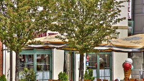 A café with outdoor seating, a large ice cream cone sculpture, and a building with a green door and windows. - Hotel am Markt (Altentreptow)