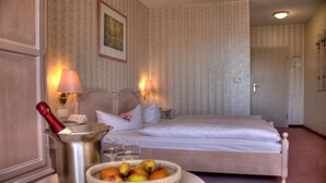 A hotel room with a bed, two bedside lamps, a nightstand with a lamp, a bowl of fruit, and a bottle of champagne. - Hotel am Markt (Altentreptow)