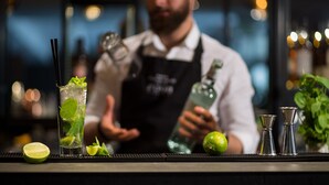 A bar setting with a bartender preparing a drink, a lime, and a bottle of liquor on the counter. - Hotel Ascot Premium (Kraków)