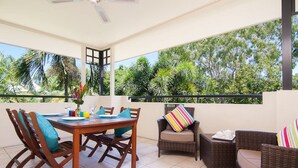 A covered outdoor dining area with a table set for two, surrounded by wicker chairs with cushions. - Mowbray by the Sea (Port Douglas)