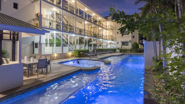 A multi-story hotel with a swimming pool, outdoor seating, and a well-lit balcony area. - Mowbray by the Sea (Port Douglas)