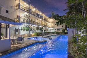 Un hôtel à plusieurs étages doté d’une piscine, d’un espace extérieur aménagé et d’un balcon bien éclairé.
