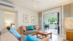A modern living room with a sofa, armchairs, and a coffee table. There is a door leading to a balcony with outdoor furniture. - Mowbray by the Sea (Port Douglas)