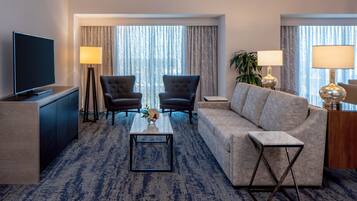 A hotel room with a flat-screen TV, two armchairs, a sofa, a coffee table, and two lamps.
