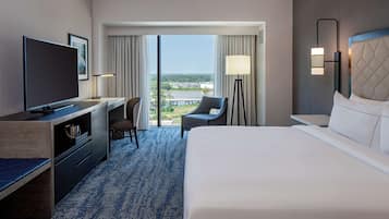 Habitación de hotel con una cama grande, un escritorio con televisor de pantalla plana, una silla, una lámpara y vistas a la ciudad desde la ventana.