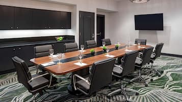 A conference room with a long table, black chairs, and a flat-screen TV on the wall.