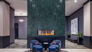 A lobby with a fireplace, two blue armchairs, a round table, and a patterned rug. - Hilton Shreveport (Shreveport)