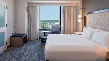 Habitación de hotel con una cama grande, un escritorio pequeño, una silla, vista a la ciudad y cortinas.