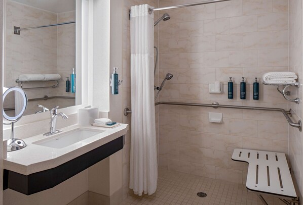 Un baño moderno con ducha, lavamanos, espejo y barras de apoyo.
