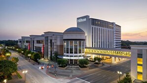 A modern hotel with a prominent Hilton sign, a convention center, and a well-lit street at dusk. - Hilton Shreveport (Shreveport)