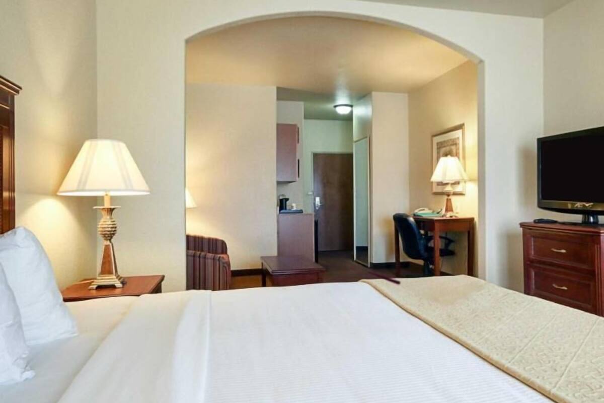 A hotel room with a bed, a desk, a chair, a television, and a lamp.