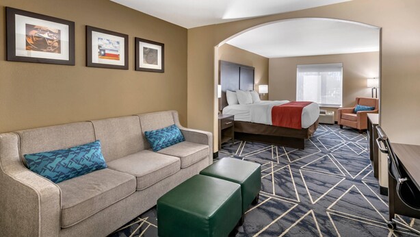 A hotel room with a bed, a sofa, a coffee table, and a desk. There are framed pictures on the wall and a window with a view. - Comfort Inn & Suites Lubbock West (Lubbock)