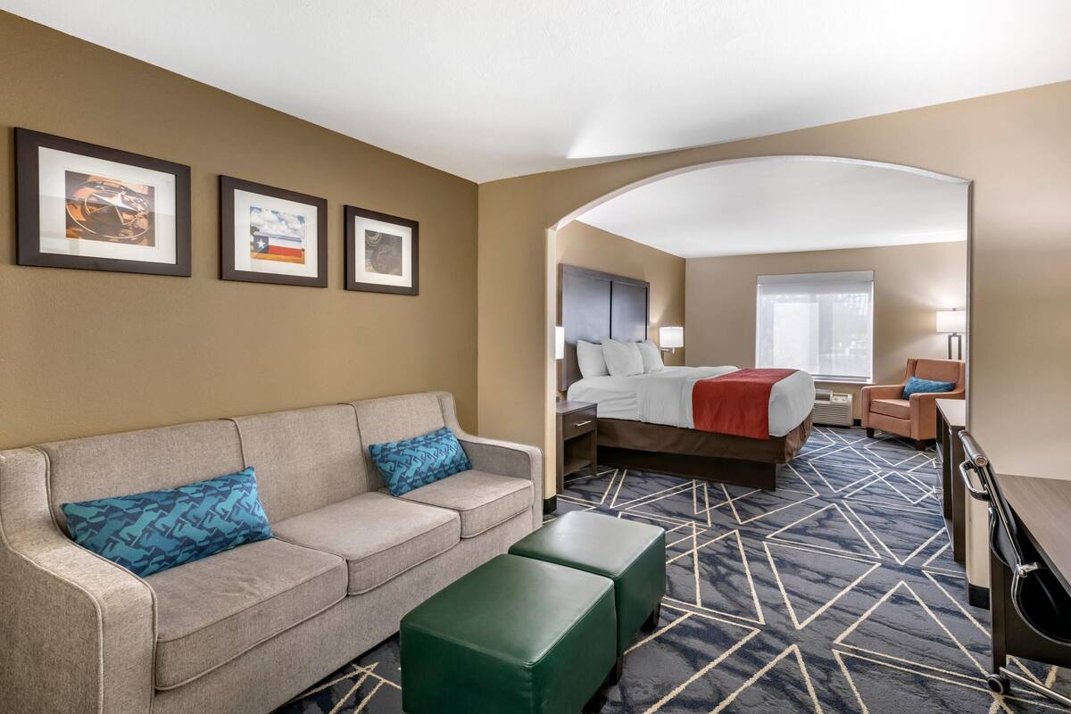 A hotel room with a bed, a sofa, a coffee table, and a desk. There are framed pictures on the wall and a window with a view.