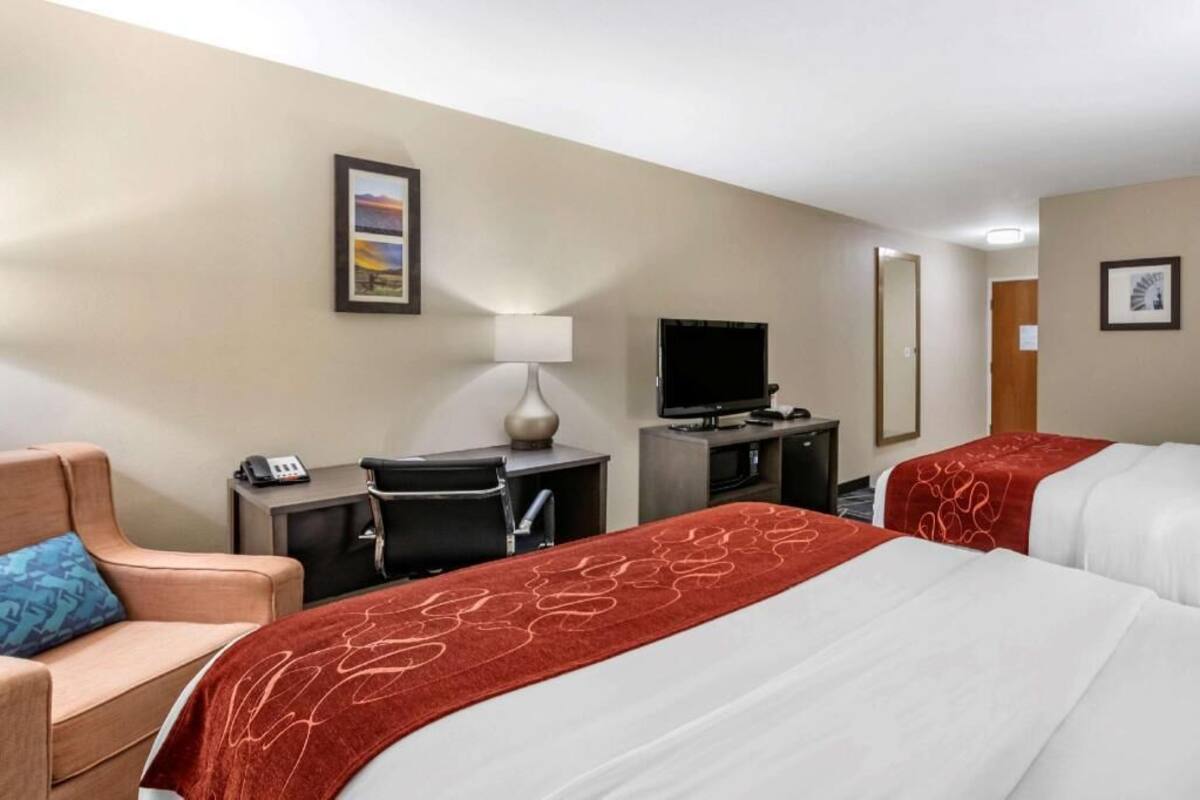 A hotel room with two beds, a desk, a chair, a TV, and a lamp.