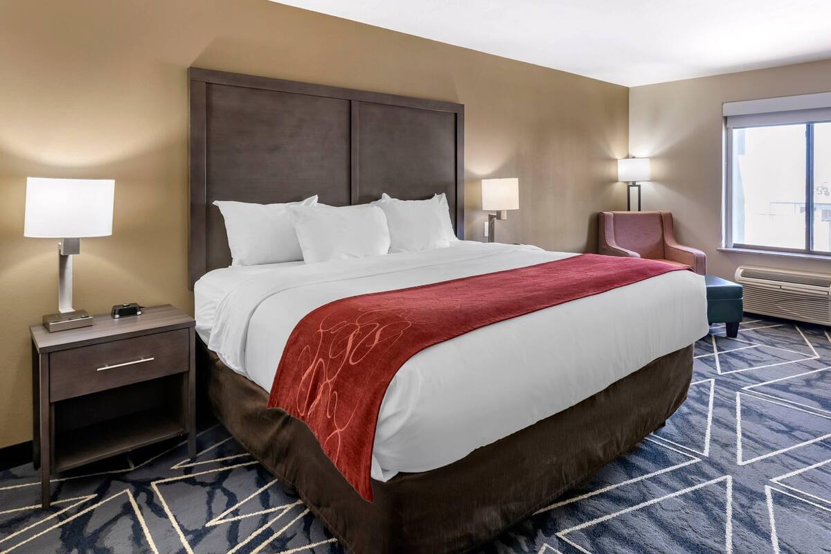 A hotel room with a large bed, two bedside tables with lamps, a chair, and a large window.