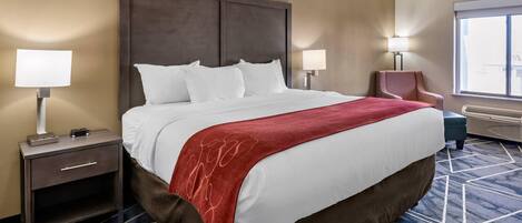 A hotel room with a large bed, two bedside tables with lamps, a chair, and a large window.