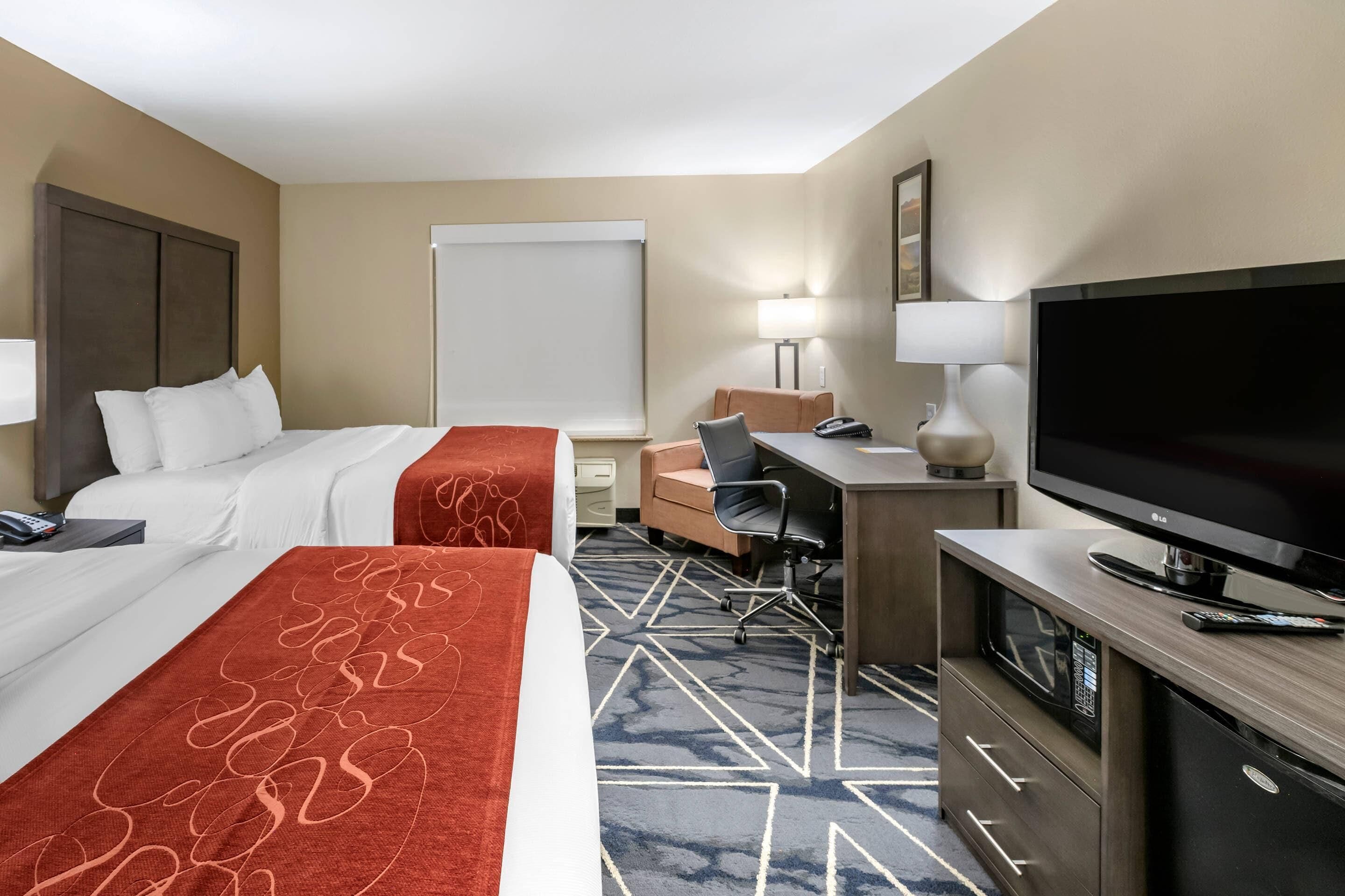 A hotel room with two beds, a desk with a TV, a chair, and a lamp.
