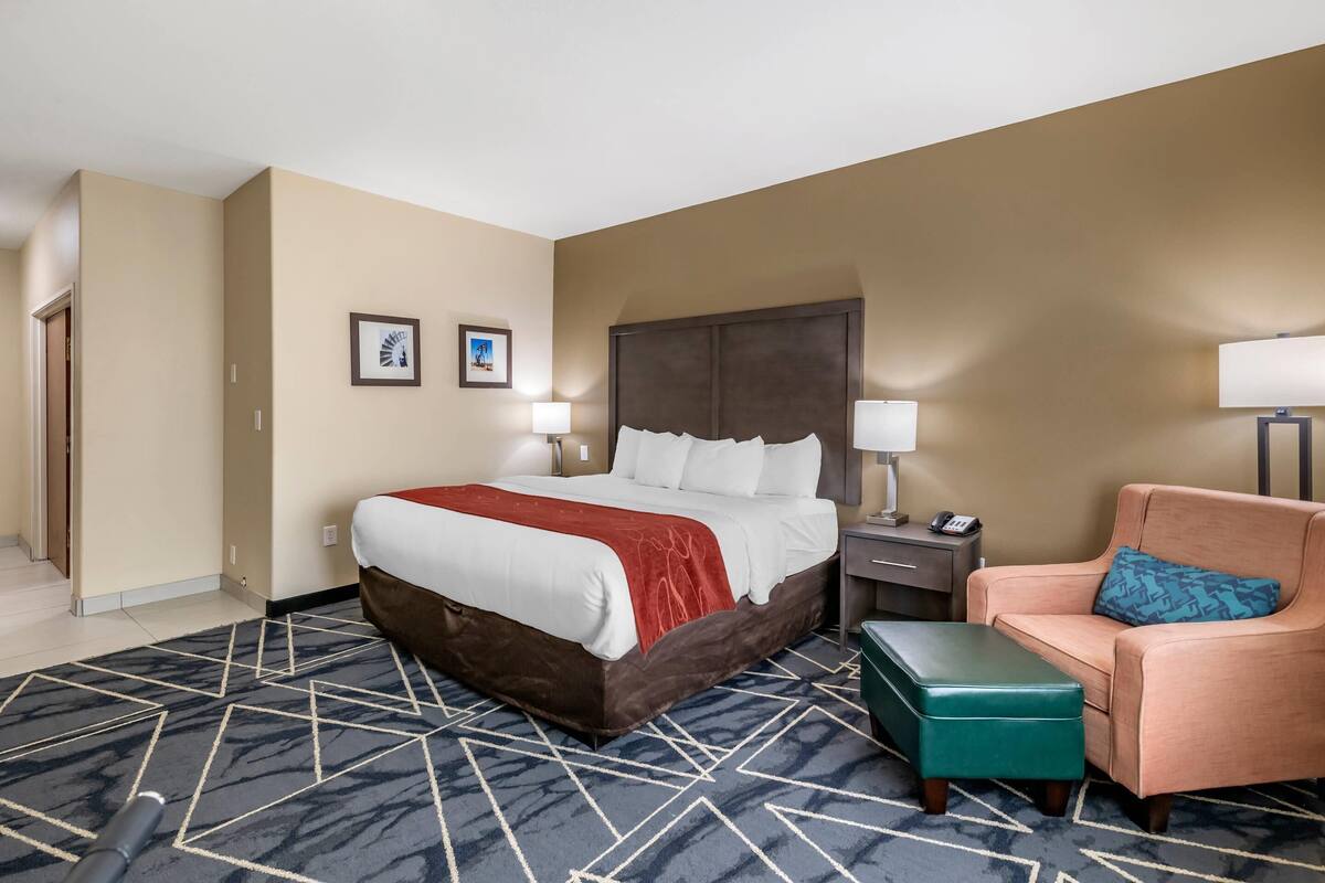 A hotel room with a large bed, a sofa, a small table, and two bedside lamps.