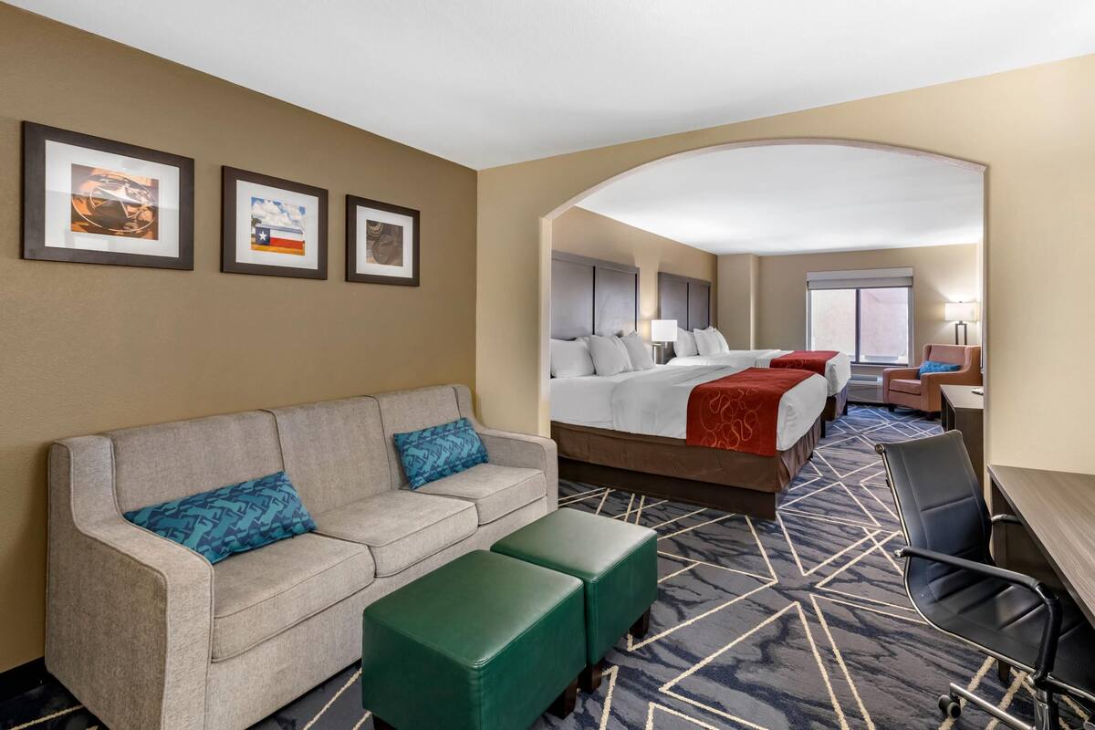 A hotel room with a bed, a sofa, a desk, and a chair. There are three framed pictures on the wall.
