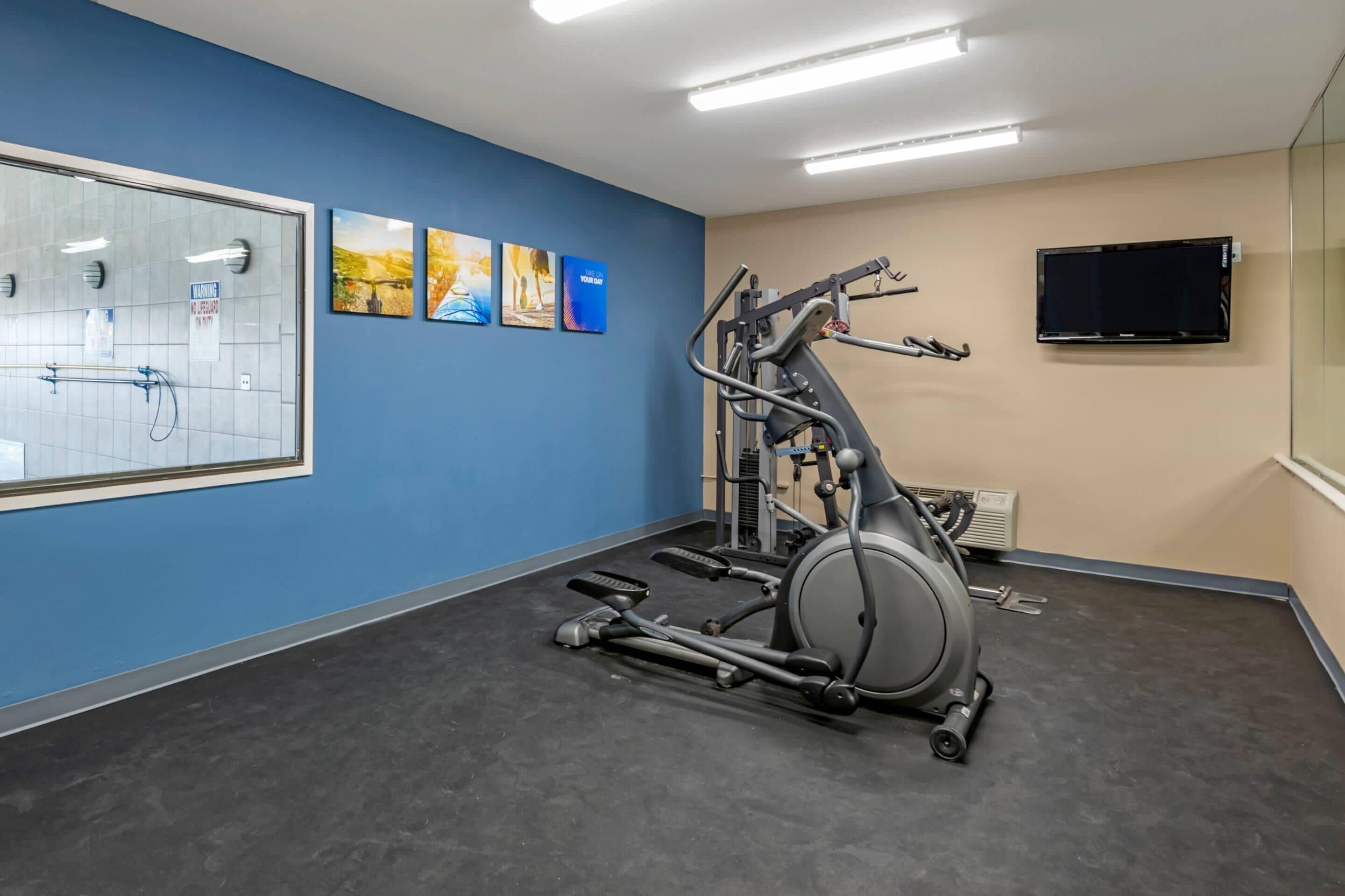 A gym with exercise equipment, a large mirror, and artwork on the walls.