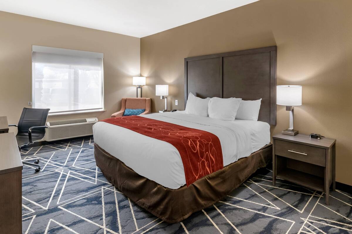 A hotel room with a large bed, a desk, a chair, and two bedside tables with lamps.