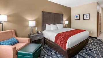 A hotel room with a large bed, a green ottoman, a sofa, a nightstand, and two wall-mounted lamps.