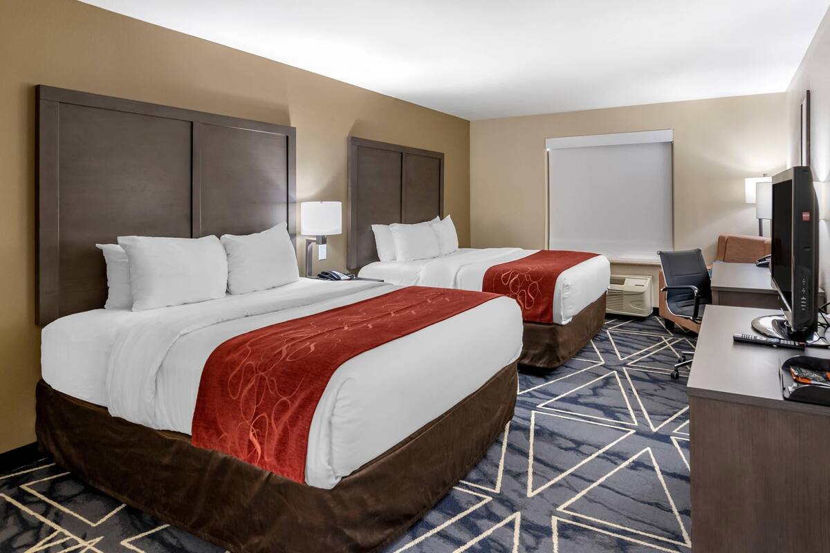 A hotel room with two beds, a desk, a chair, and a television.