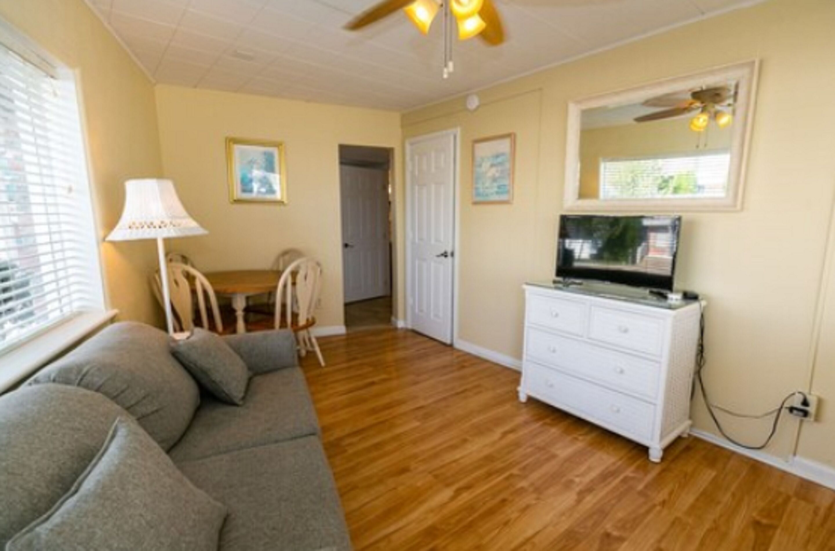 A room with a sofa, a TV on a dresser, a ceiling fan, and a door leading to another room.