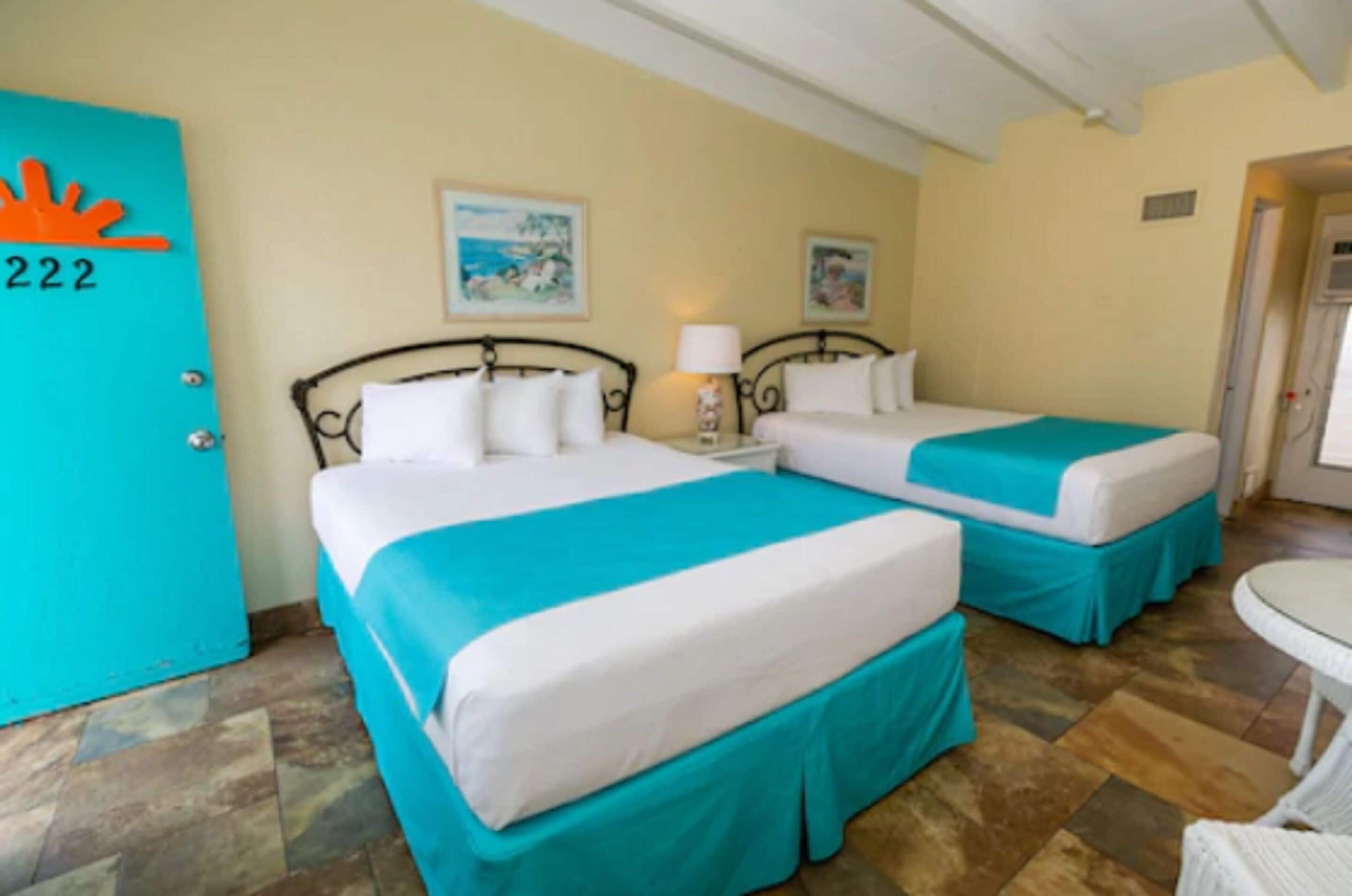 A hotel room with two beds, a small table, and a door marked with the number 222.