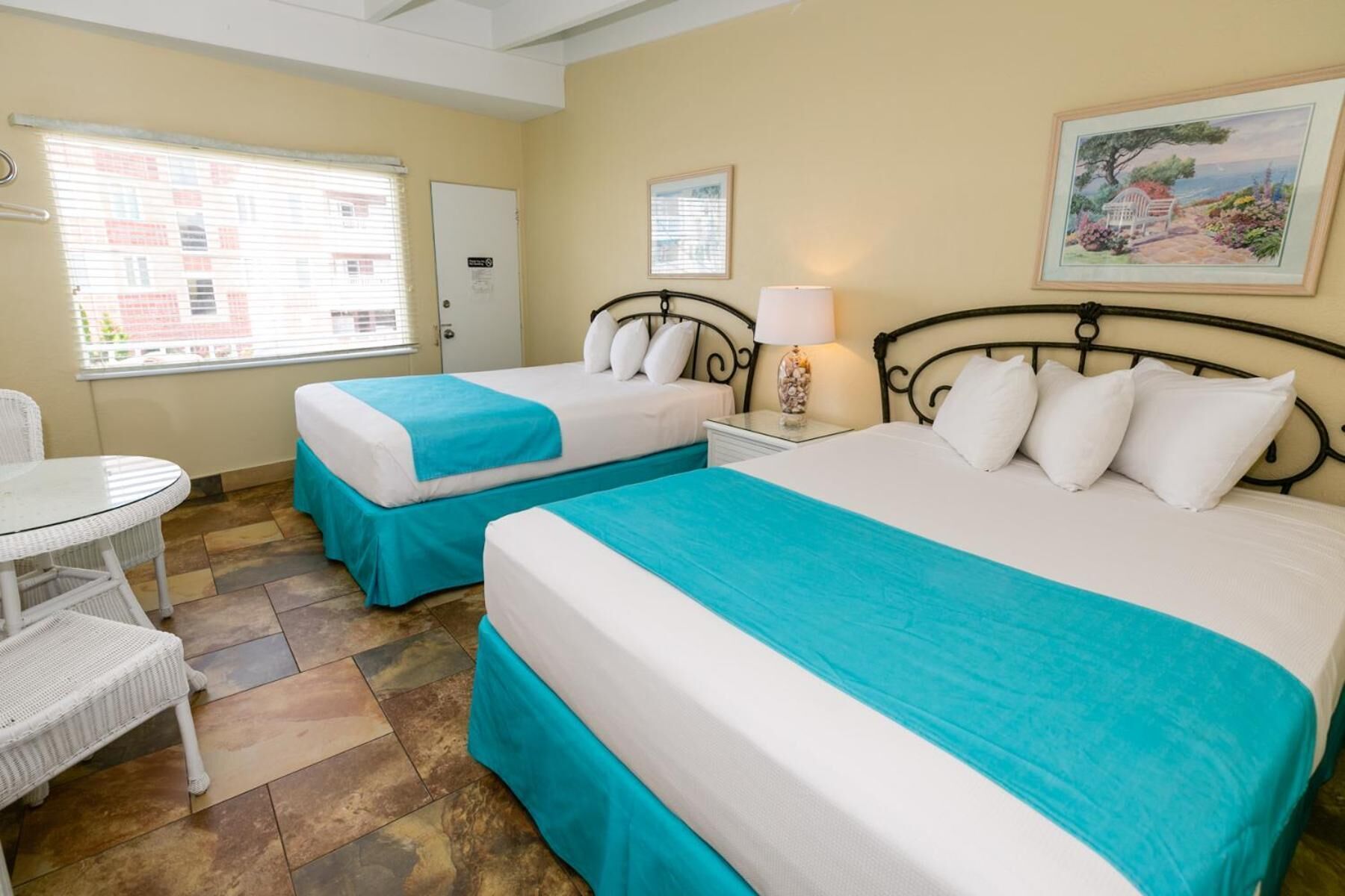 A hotel room with two beds, a small table, and a chair.
