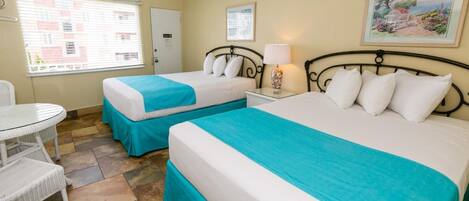 A hotel room with two beds, a small table, and a chair.