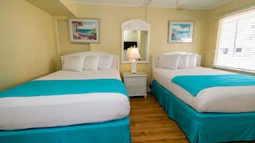 A room with two beds, each with a white mattress and teal bedspread, a nightstand with a lamp, and a window with blinds.
