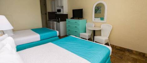 A hotel room with two beds, a kitchenette, a small table with a chair, and a mirror on the wall.