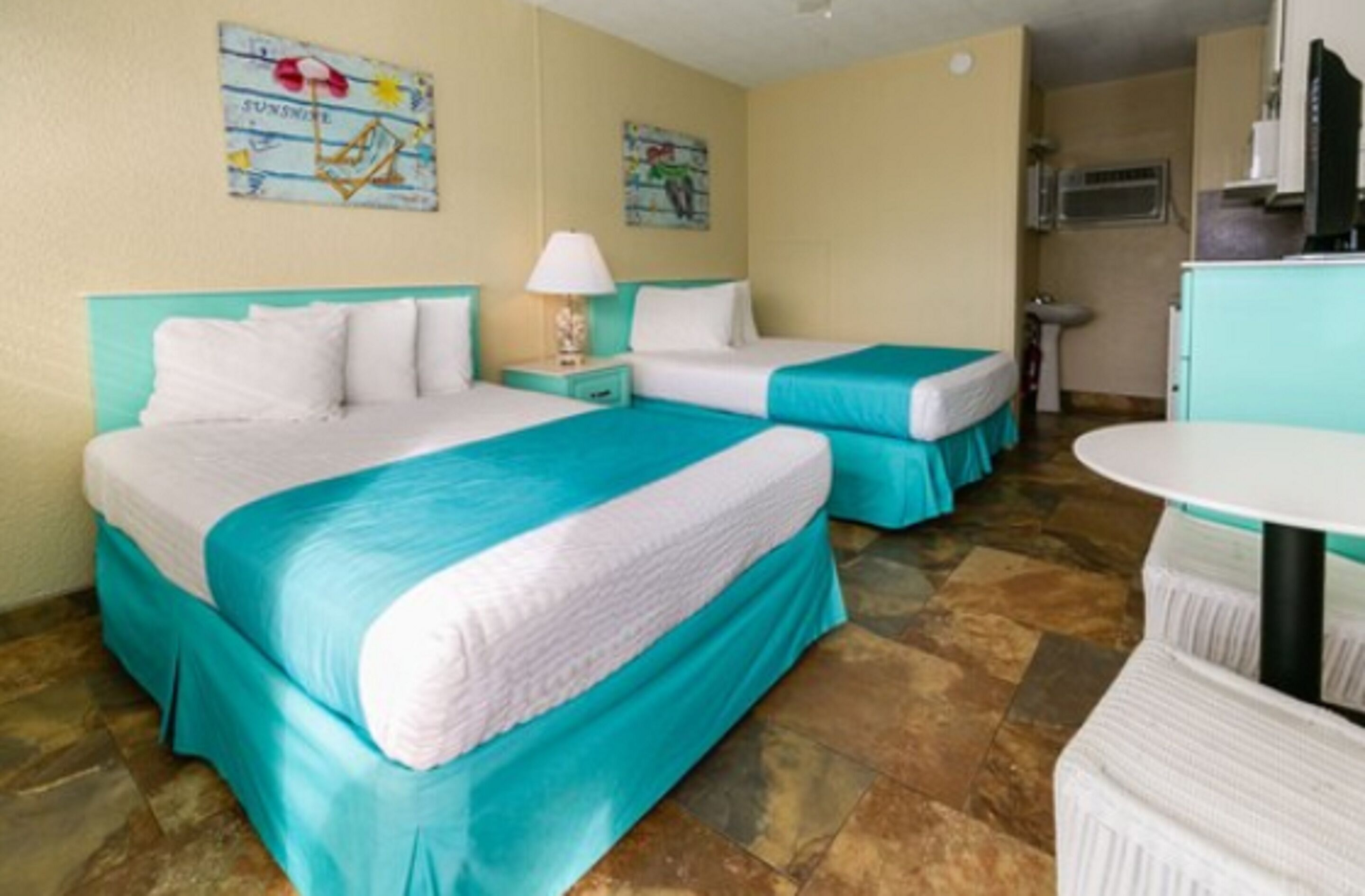 A hotel room with two beds, a small kitchenette, and a dining area.