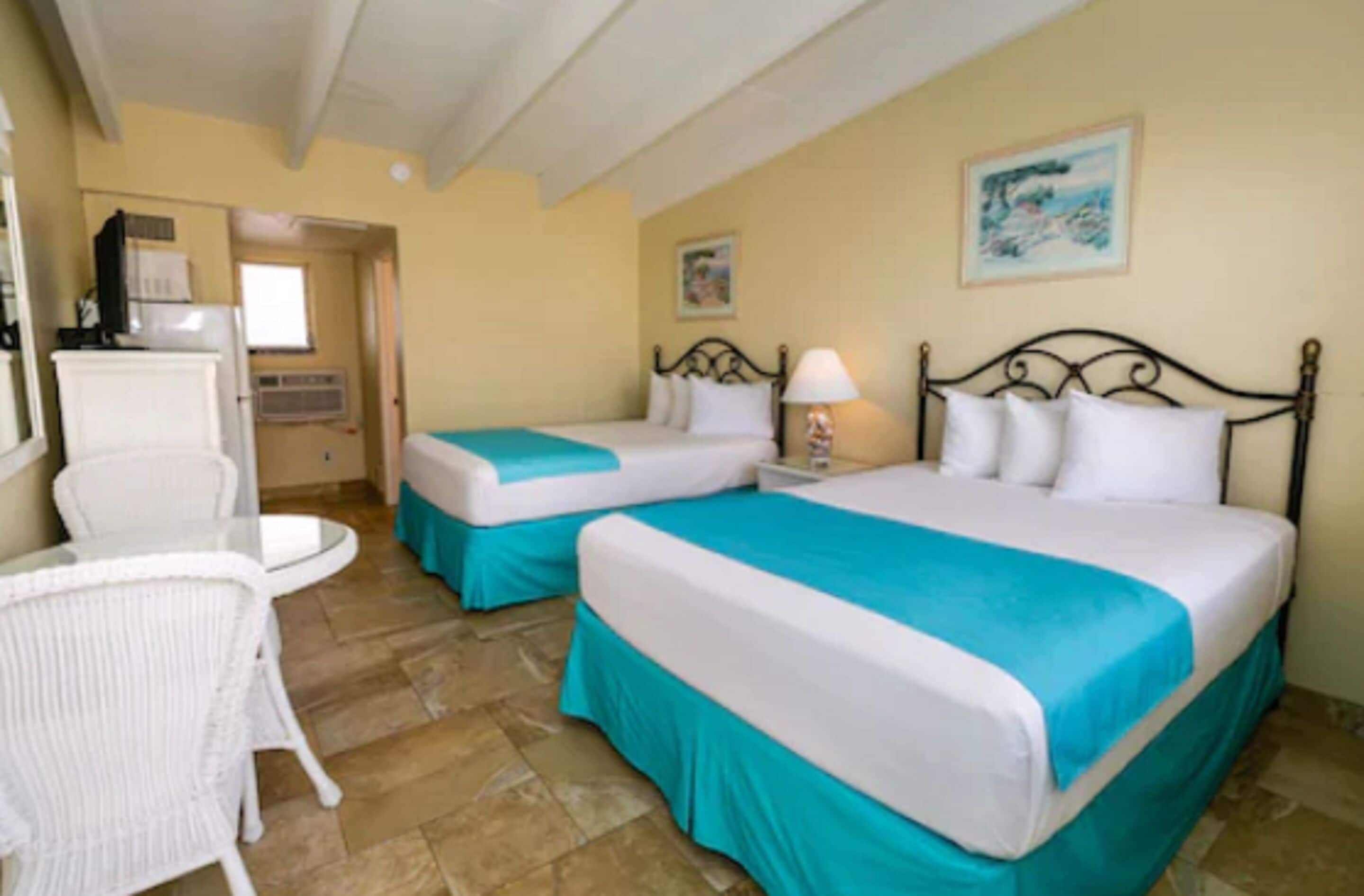 A hotel room with two beds, a small table, a chair, and a window.