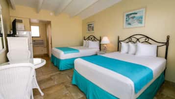A hotel room with two beds, a small table, a chair, and a window.