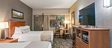 Habitación de hotel con dos camas, un televisor, un escritorio con lámpara y vista al exterior.