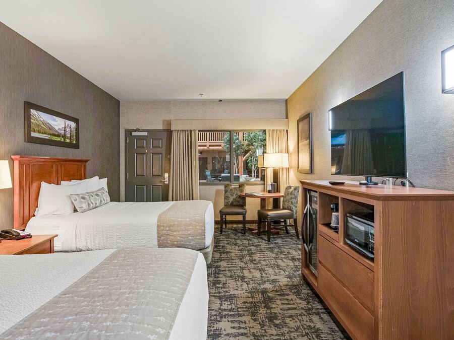 Habitación de hotel con dos camas, un televisor, un escritorio con lámpara y vista al exterior.