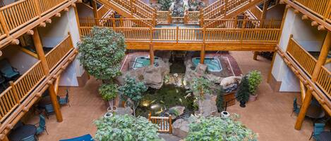A multi-level atrium with wooden railings, indoor plants, and a central water feature.
