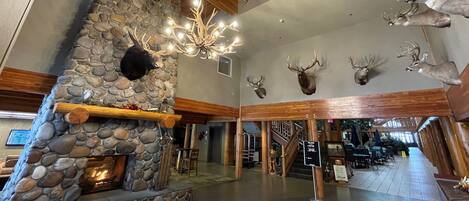 A lobby with a stone fireplace, wooden beams, and mounted deer heads.