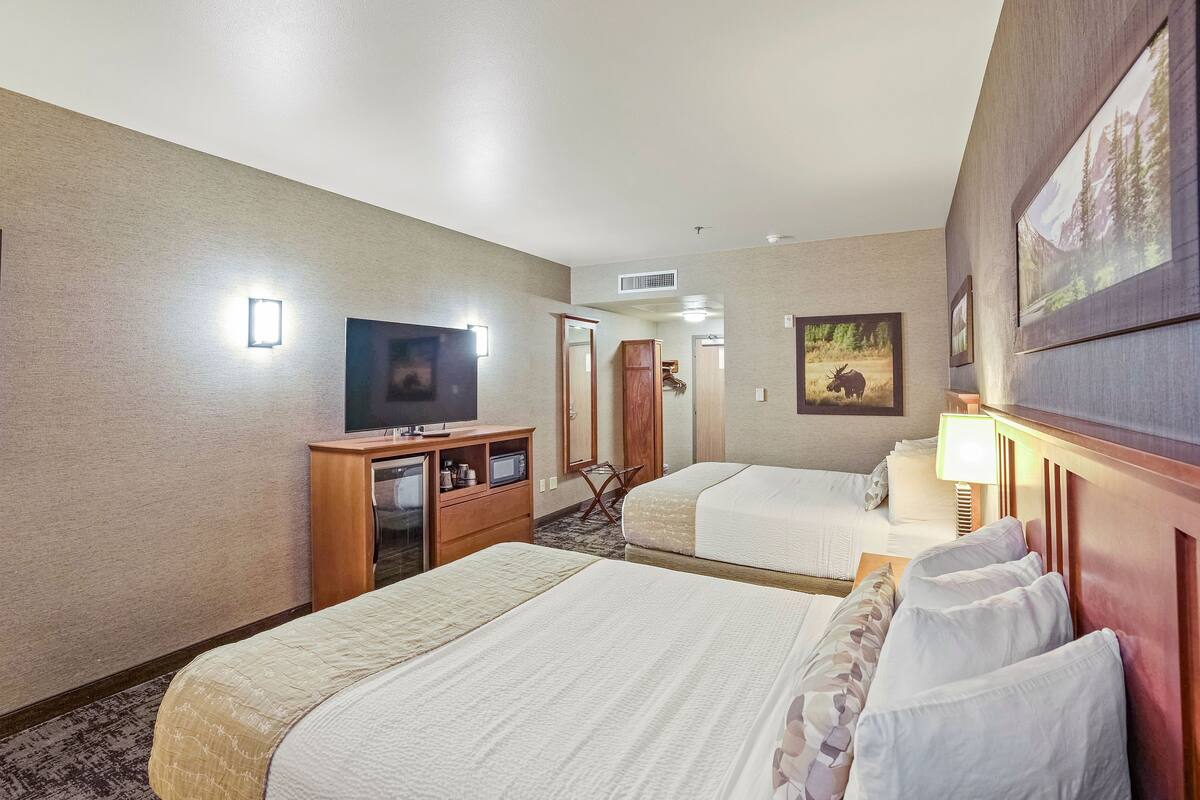 A hotel room with two beds, a TV, a desk with a computer, and a mirror.