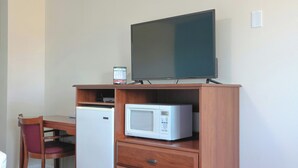 Una kitchenette equipada con microondas, refrigerador y televisor sobre un mueble de madera.