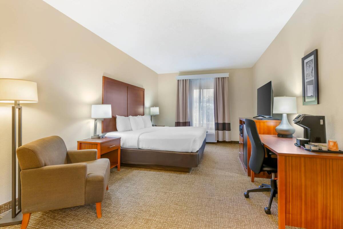 A hotel room with a bed, a desk, a chair, and a lamp.