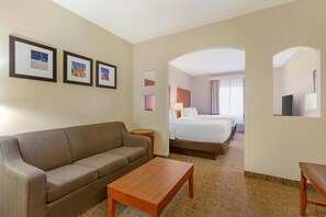 A hotel room with a sofa, a wooden table, a bed, and framed pictures on the wall. - Comfort Inn & Suites Socorro (Socorro)