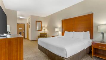 A hotel room with a large bed, wooden headboard, a desk with a computer, and a chair.